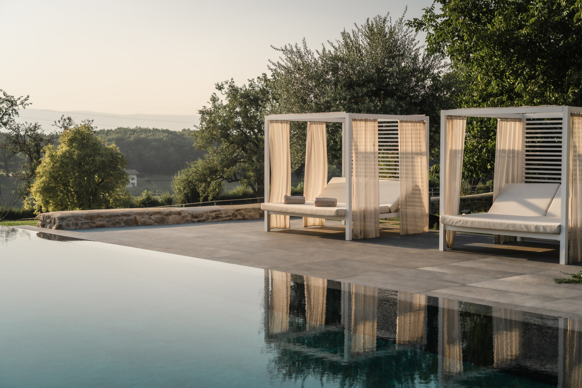Lits de repos à baldaquin et rideaux de lin au bord d'une piscine à débordement au lever du soleil