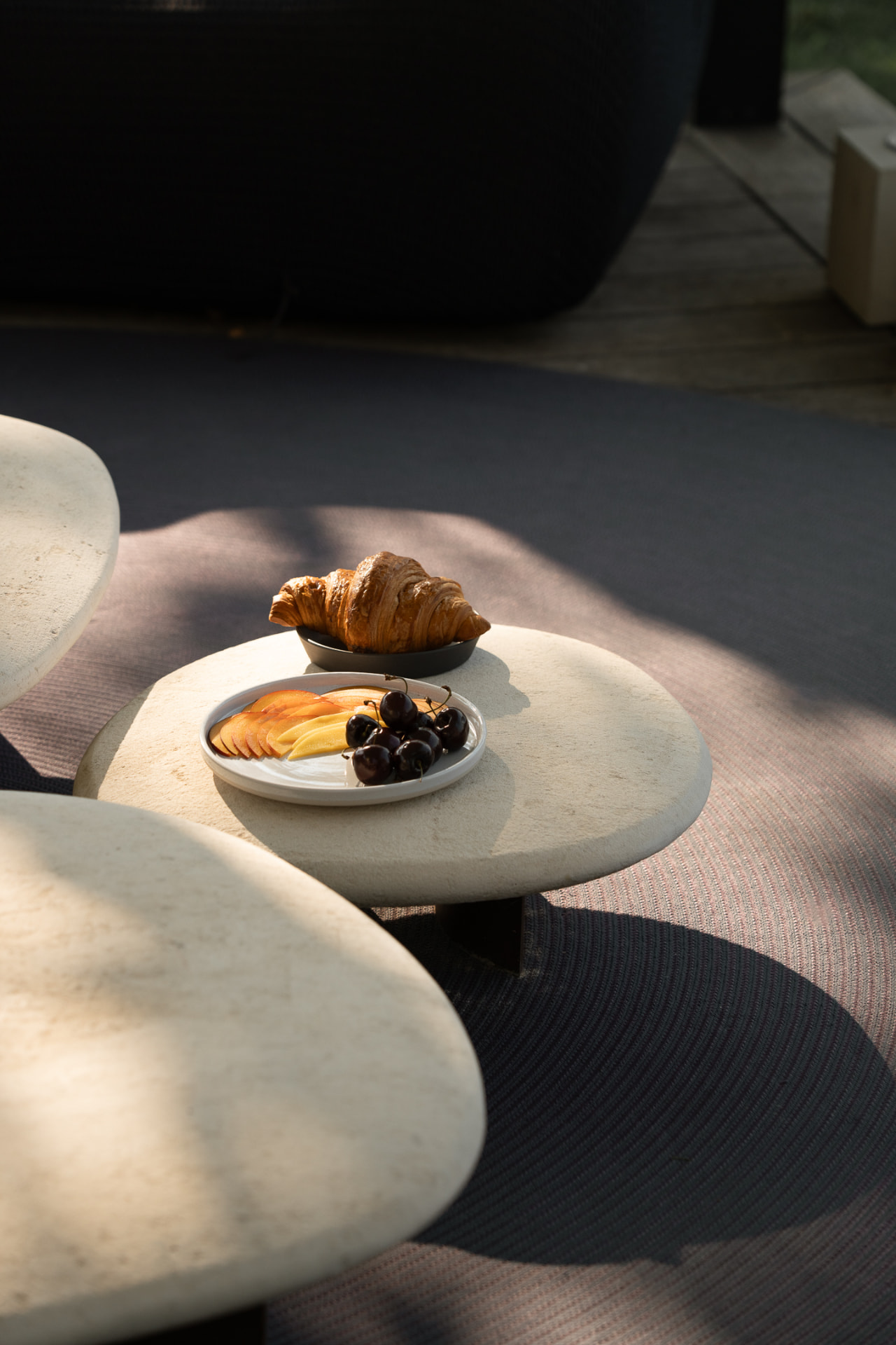 Croissant et assiette de fruits sur des tables basses en pierre, lumière rasante du matin