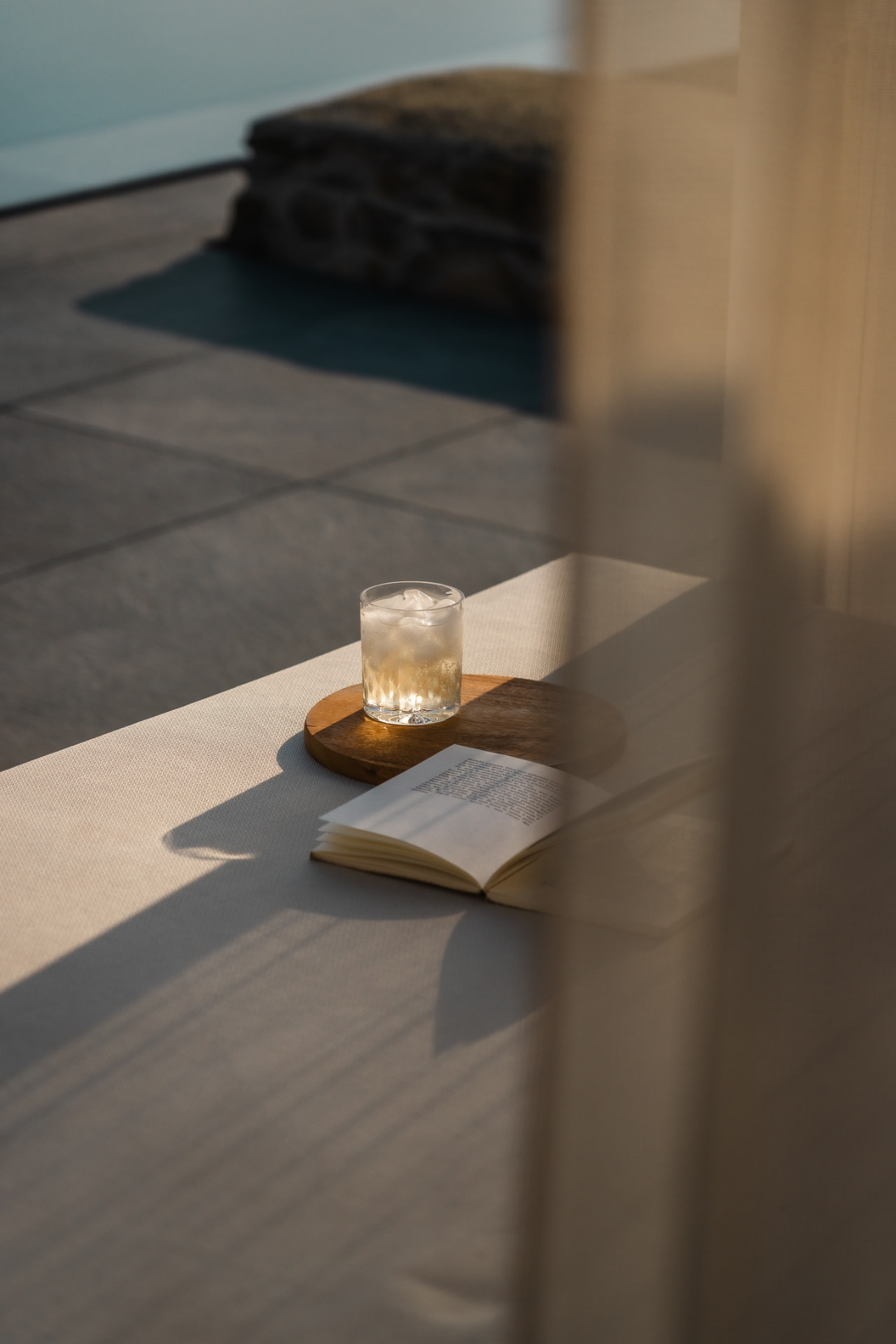 Verre et livre sur une banquette, vue plongeante vers la piscine à travers un voilage