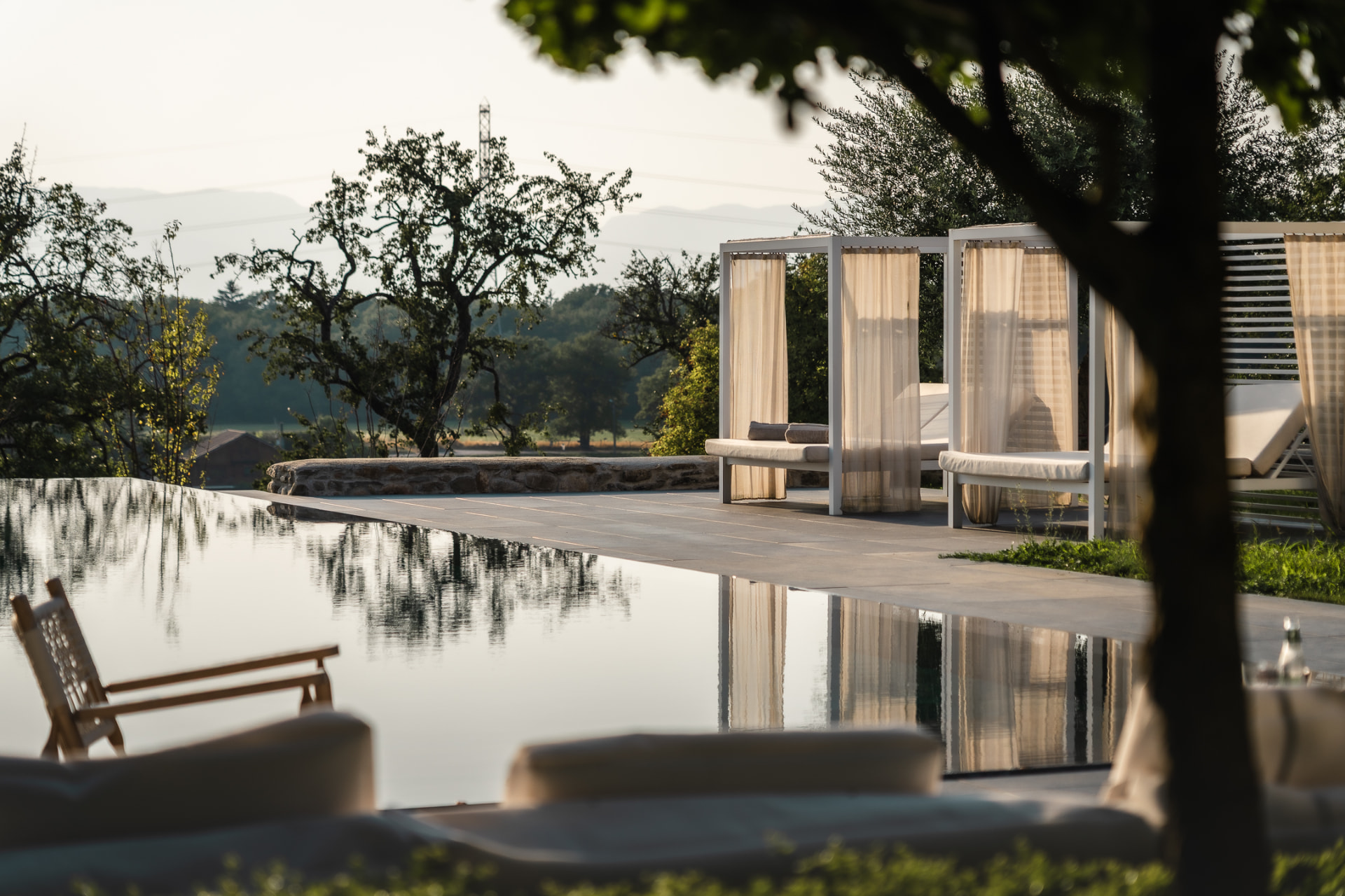 Reflet des cabanes de piscine et des oliviers dans l'eau immobile, au coucher du soleil